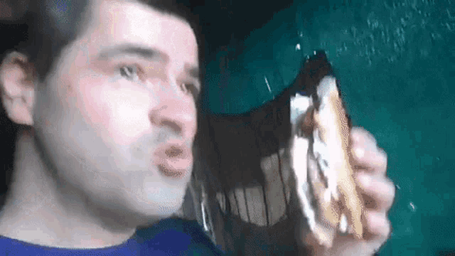 a man in a blue shirt is eating a sandwich with a bite taken out of it .