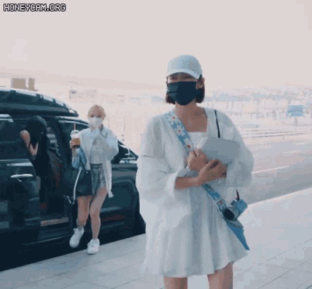 a woman wearing a mask is standing next to another woman wearing a hat