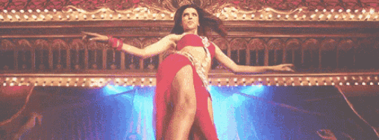 a woman in a red dress is dancing on a stage with lights behind her .