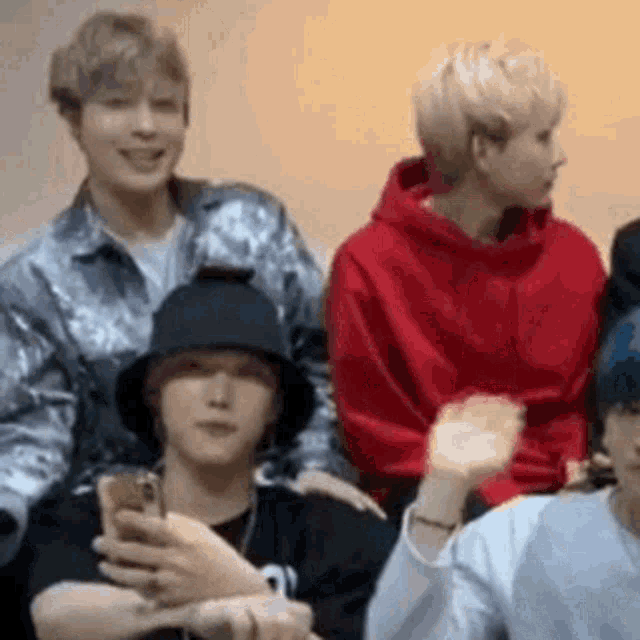 a group of young men are sitting in a room . one of the men is holding a cell phone .