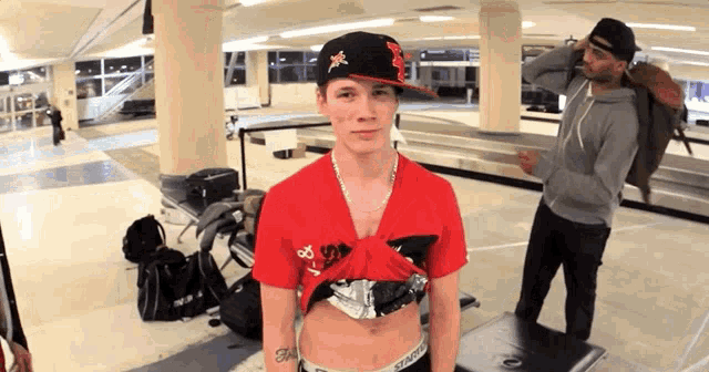 a man wearing a red shirt and a black hat with the letter m on it looks at the camera