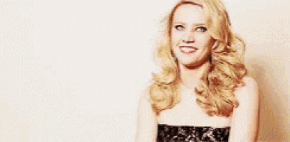 a blonde woman in a black dress is smiling and looking at the camera .