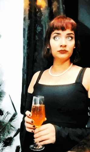 a woman in a black dress is holding a glass of orange liquid
