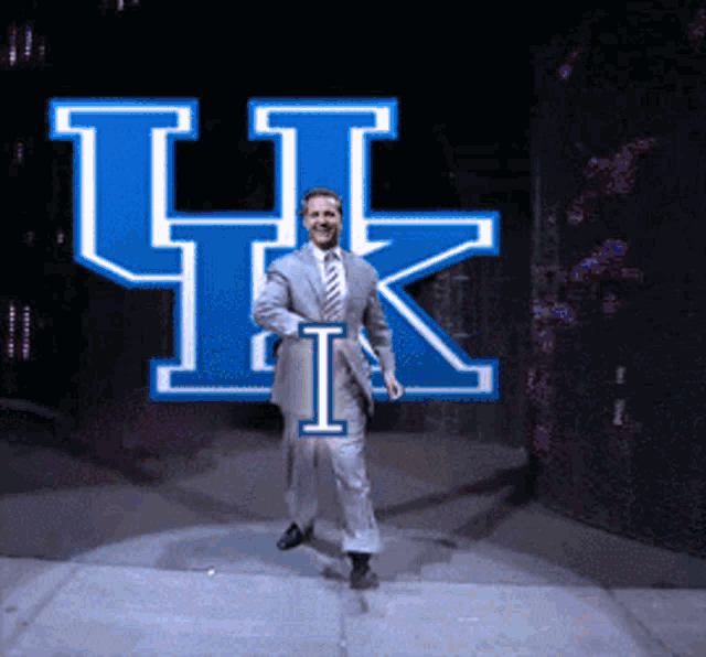 a man in a suit and tie is dancing in front of a large blue uk logo