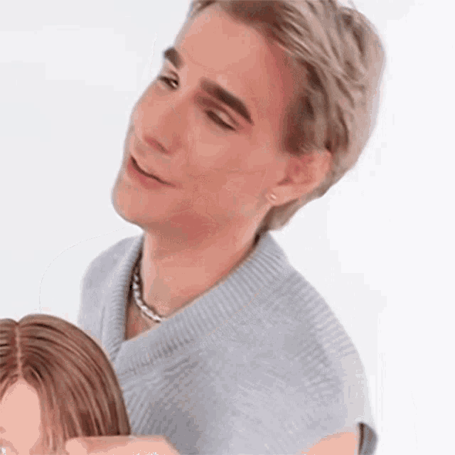a man in a grey sweater is holding a mannequin 's head .