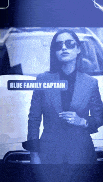 a woman in a suit and sunglasses stands in front of a white car with the name blue family captain displayed