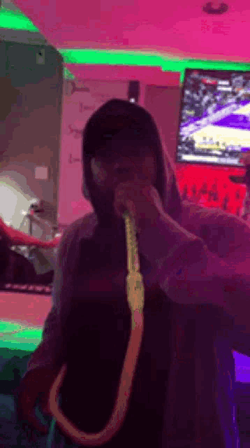 a man in a hoodie is smoking a hookah in a room with purple and green lights .