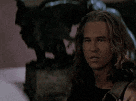 a man with long hair looks at the camera in a dark room