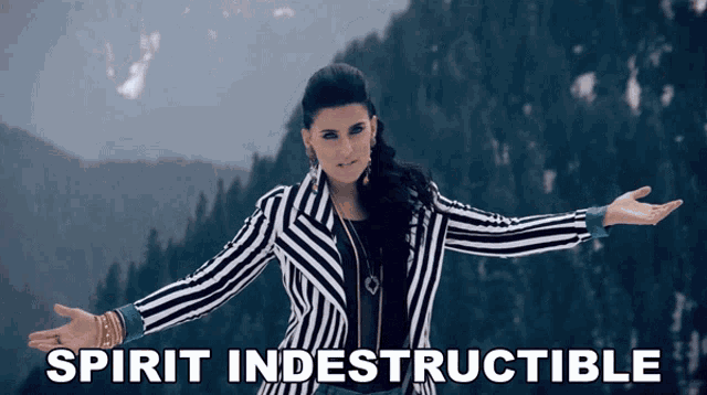 a woman in a striped jacket stands in front of a mountain with the words spirit indestructible written below her
