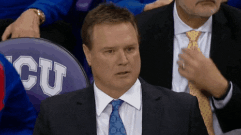 a man in a suit and tie sits in front of a seat that says cu on it