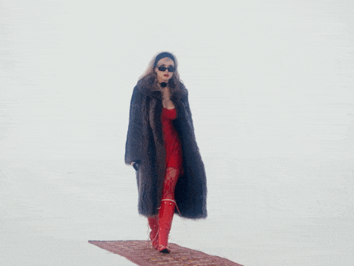 a woman wearing a fur coat and sunglasses is holding a gun