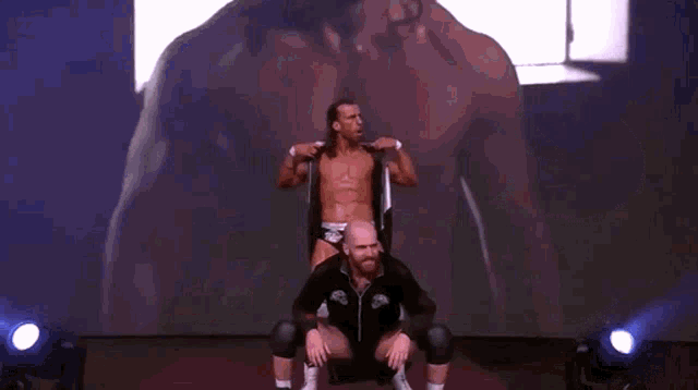 a wrestler is sitting on another wrestler 's shoulders with the letter r on his chest .