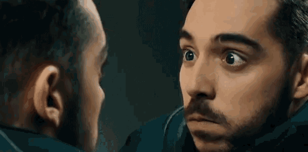a man with a beard is looking at his face in a mirror