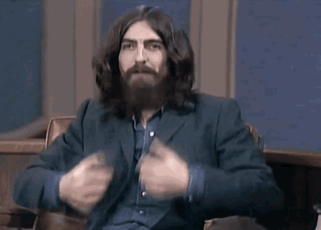 a man with long hair and a beard is sitting in a chair and talking .