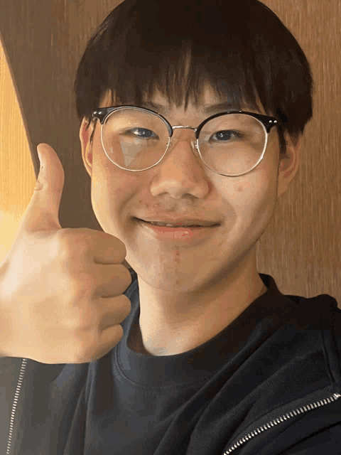 a young man wearing glasses gives a thumbs up sign