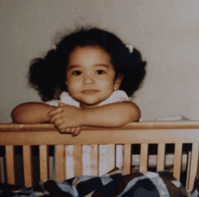 a little girl sitting in a wooden crib with her head on the railing