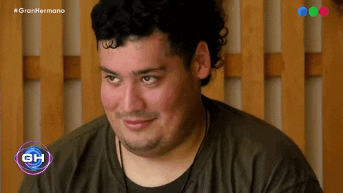 a man with curly hair is smiling in front of a wooden wall .