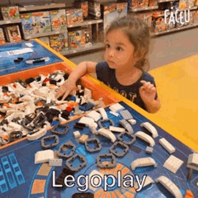 a little girl is sitting at a table filled with lego blocks .