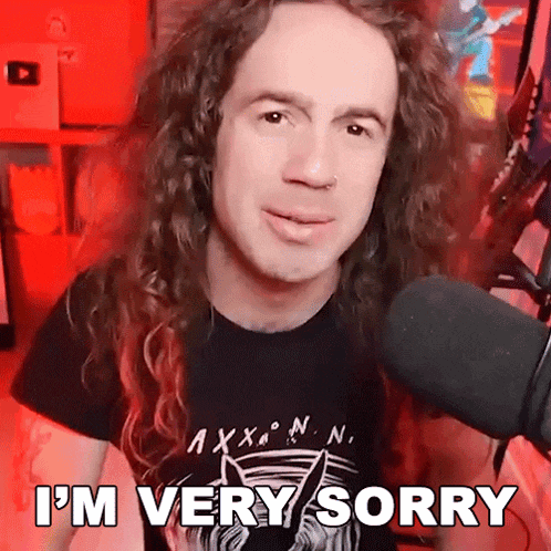 a man with long curly hair is standing in front of a microphone and saying i 'm very sorry
