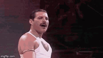 a man with a mustache and a white tank top is standing in front of a red background .