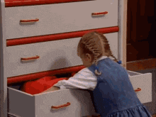 a little girl is reaching into a dresser drawer with a red handle