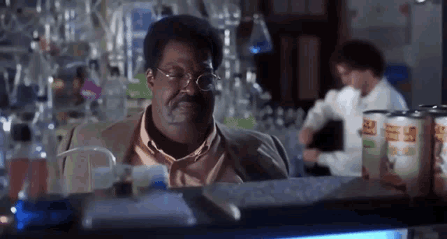 a man wearing glasses is sitting at a table in a laboratory .