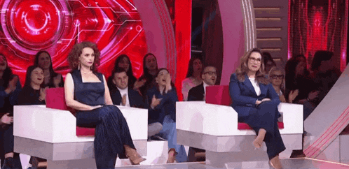 two women are sitting in chairs in front of a crowd of people applauding .