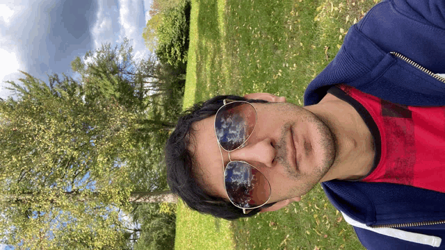 a man wearing sunglasses and a red shirt stands in a park