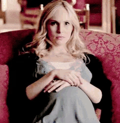 a woman in a blue dress is sitting in a red chair with her legs crossed .