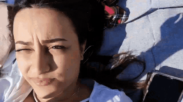a woman is laying on a blanket with her eyes closed and a cell phone in her hand .