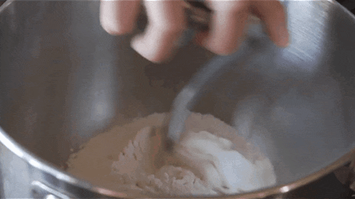 a person is mixing flour in a metal bowl with a spoon .