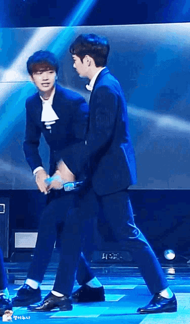 two men in suits are standing on a stage holding hands .