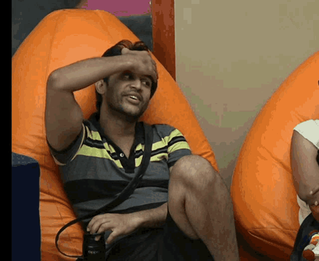 a man in a striped shirt sits on an orange bean bag chair
