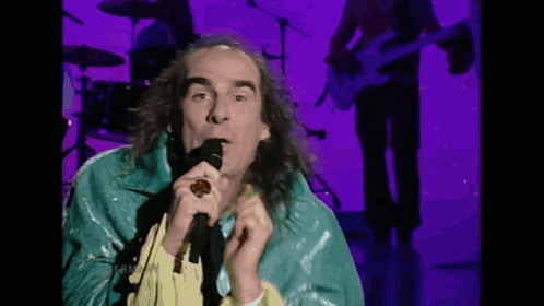 a man singing into a microphone with a ring on his finger in front of a purple background