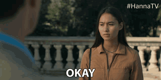 a woman in a brown jacket says okay in front of a railing