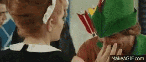 a man and a woman are standing next to each other . the man is wearing a green hat with arrows on it .