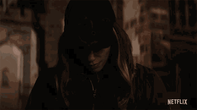 a close up of a woman wearing a black hat and a black jacket with netflix written on the bottom