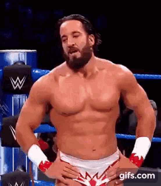 a shirtless wrestling wrestler is standing in a ring with his hands on his hips .