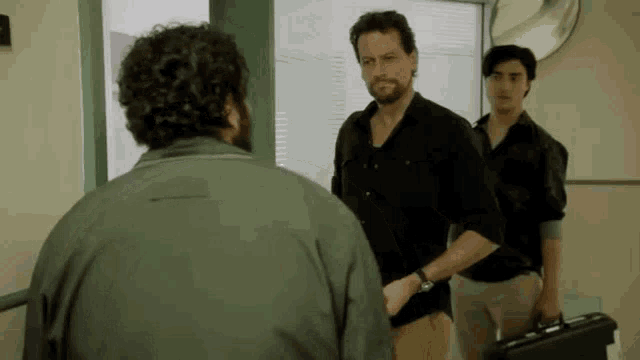 a group of men are standing in a room talking to each other