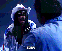 a man wearing a cowboy hat is talking to another man and says slap