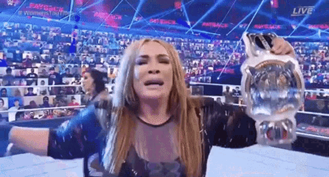 a woman is holding a wrestling championship belt in front of a crowd of people .