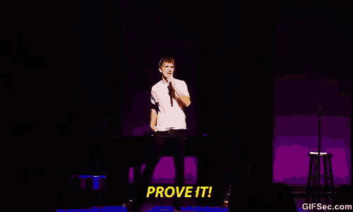 a man is standing on a stage holding a microphone and saying prove it
