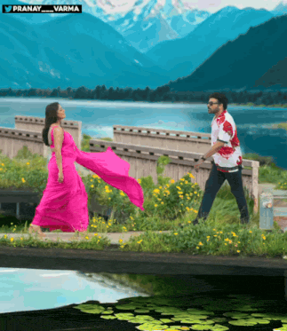 a woman in a pink dress is walking across a bridge with a man in a white shirt