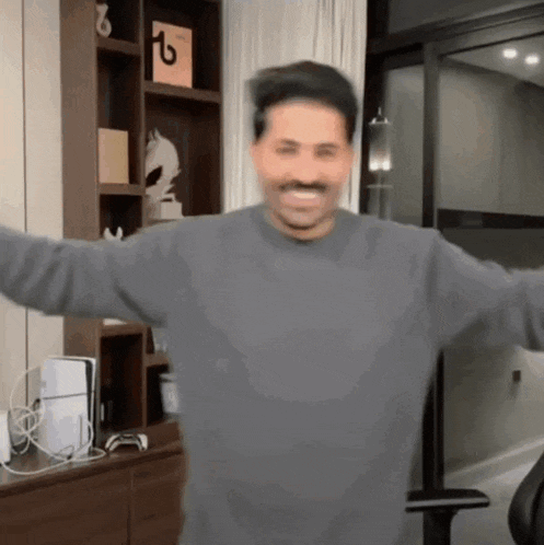 a man in a grey sweater is standing in a room with his arms outstretched