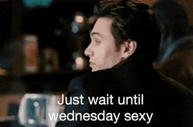 a man is sitting at a bar with the words `` just wait until wednesday sexy '' on his face .