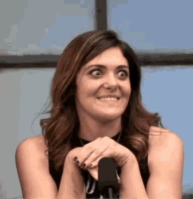 a woman sitting in front of a microphone with her hands folded in front of her face