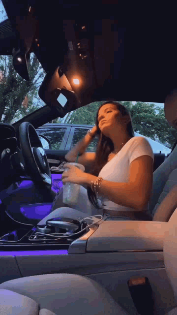 a woman is sitting in the driver 's seat of a car holding a cup of coffee .