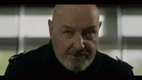 a bald man with a beard is looking at the camera in a dark room .