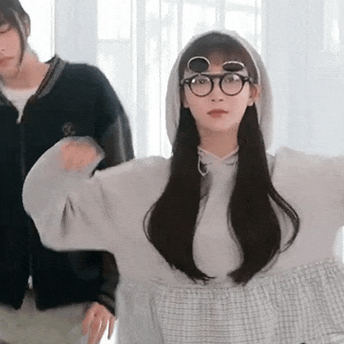 a girl wearing glasses and a hoodie is standing next to a man wearing a jacket .