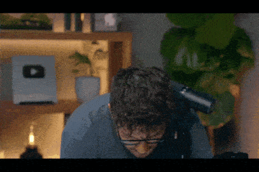 a man sitting in front of a microphone with a youtube logo on the shelf in the background